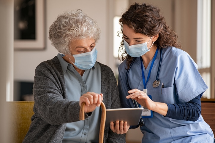 An elderly woman at a care facility uses a tablet with the assistance of a care aide