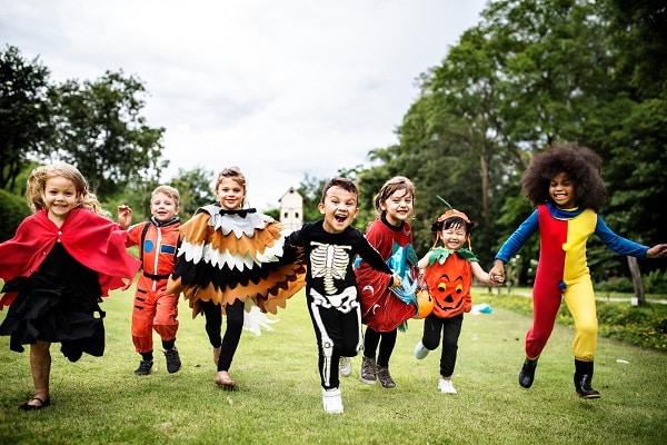 A group of costumed children running through the grass on Halloween