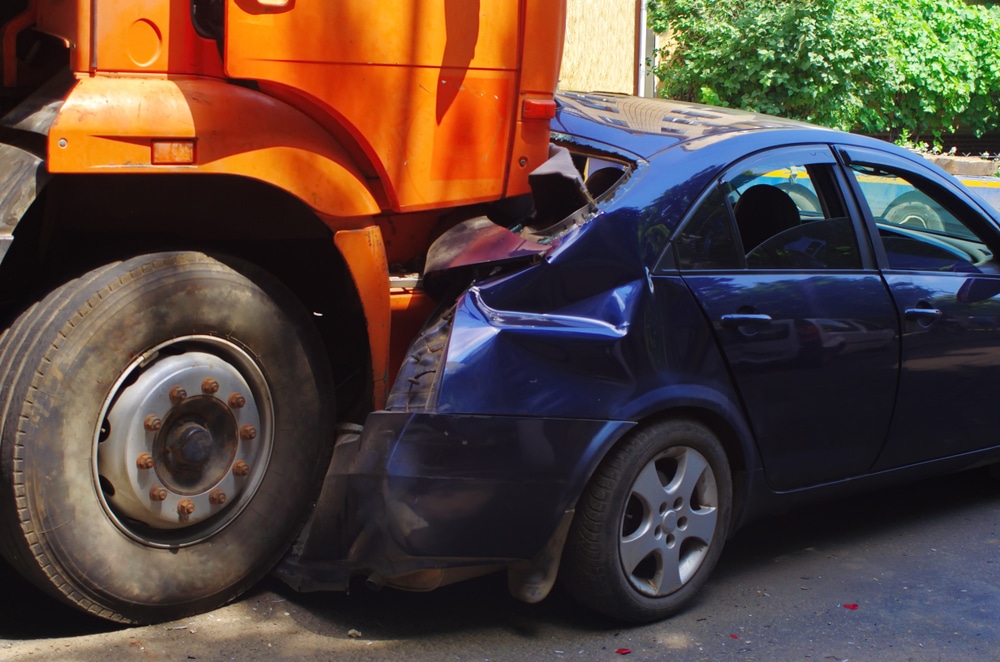 Orange tractor-trailer rear ends a blue car on the road. The driver of the car should consult with a lawyer.