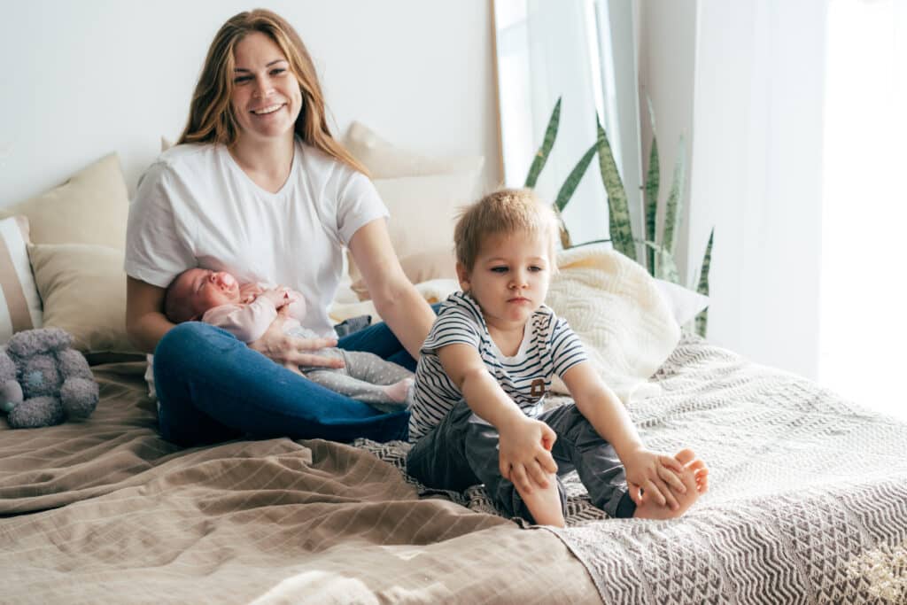 Mom on bed holding her baby, unaware of the abuse her older child has suffered